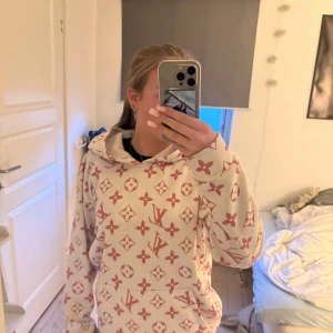 Vit och rosa Louis Vuitton hoodie - Säljer en vit hoodie från Louis Vuitton med rosa monogramtryck över hela tröjan. Hoodien har huva, känguruficka och långa ärmar. 