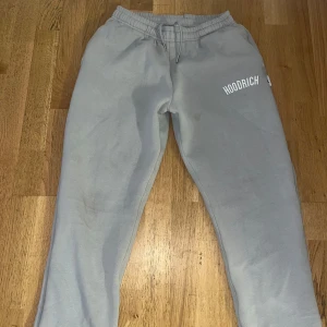 Grå mjukisbyxor från Hoodrich M - Grå mjukisbyxor från Hoodrich i storlek M. Byxorna har elastisk midja med snörning och tryckt Hoodrich-logga på vänster ben. Tillverkade i mjukt bomullsmaterial för maximal komfort och avslappnad stil.