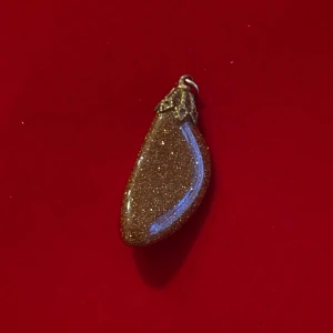 Glittrigt brunt halsbandshänge - Unikt halsbandshänge i droppformad design med glittrig brun yta och guldfärgad metallfattning. Perfekt för dig som vill ha ett smycke som sticker ut och ger extra shine till din look.