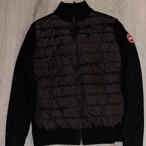 Canada Goose Hybridge Cardigan - Svart cardigan jacka från Canada Goose. Knappt använd alls helt ny bara legat i garderoben då den var för tight på mig.