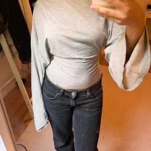  långärmad tröja med vida ärmar - Säljer en ljusgrå långärmad topp med vida ärmar och tight passform i midjan. Toppen har en clean look med rund hals och är tillverkad i mjukt bomullsmaterial. Perfekt för dig som gillar en stilren men ändå unik vibe.