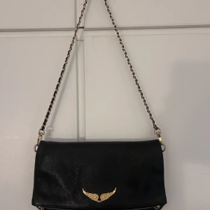Zadig & voltaire väska  - Clutch från Zadig & voltaire i svart med guldkedjor, både kort och lång kedja medföljer, väldigt varsamt använd och har mest bara hängt i garderoben senaste året, endast lite slitningar på vingarna fram men inget man ser om man inte kollar nära💗 Köpt på boozt för 3700kr för 2 år sedan , pris kan diskuteras