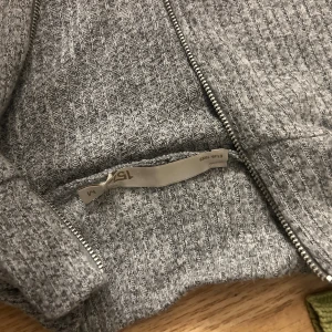 Grå ribbad kofta med dragkedja - Grå ribbad kofta från lager 157 med lång ärm och hel dragkedja framtill. Mjuk och stretchig känsla, perfekt att slänga på sig över en t-shirt. Enkel och stilren design som funkar till det mesta.