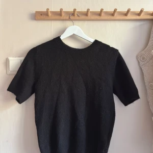 Svart stickad tröja från H&M - Svart stickad tröja från H&M i storlek XS. Tröjan har rund halsringning och korta ärmar, perfekt för lager-på-lager eller som den är. Enkel och stilren design som funkar till många olika looks. Är nopprig men har mycket kvar att ge.