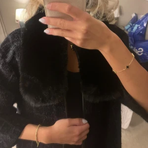 Svart kappa med fuskpäls-krage - Säljer denna så snygga  svarta långa kappan med stor, mjuk fuskpäls-krage. Jackan har rutigt mönster i tyget och trekvartsärmar. Stängs med knappar innanför och har en ”rak” passform. Använd en gång så den är som helt ny