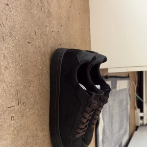 Svarta sneakers i mocka - Säljer ett par stilrena svarta sneakers med ovandel i mocka och detaljer i skinn. Skorna har svarta snören egntiligen men är lite smutsiga 