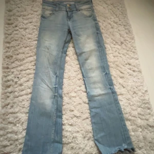 Ljusblå bootcut jeans från Bershka - Säljer ett par ljusblå jeans från Bershka med bootcut-modell och femficksdesign. Jeansen har dubbla knappar i midjan och är tillverkade i denim med slitna detaljer och lätt tvättad look.