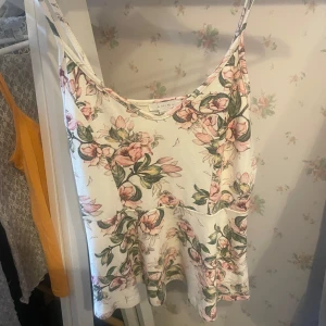 Blommig linnetopp från Amisu - Supersöt linnetopp från Amisu med smala axelband och blommigt mönster i rosa och grönt på vit botten. Toppen har en lätt utsvängd passform och är perfekt för varma dagar. Materialet känns mjukt och luftigt, vilket gör den extra skön att bära.