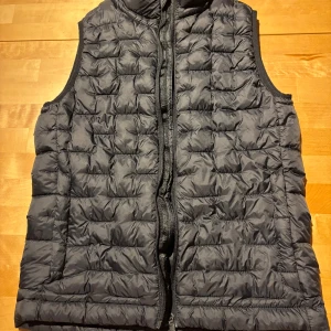 Svart väst från Everest - Säljer en svart quiltad väst från Everest i storlek 146/152. Västen har dragkedja framtill, fickor med dragkedja och en klassisk, sportig look. Perfekt att slänga över en hoodie eller tröja när det är kyligt ute. Enkel och stilren design som funkar till det mesta.
