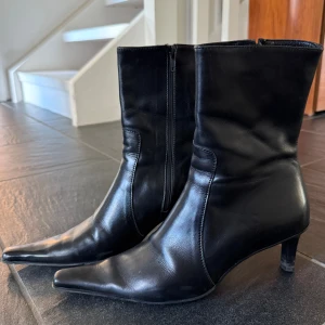 Svarta stövletter med spetsig tå - Snygga svarta Italienska stövletter i skinn med spetsig tå och klack. Skorna har dragkedja på sidan för enkel påtagning och en stilren, minimalistisk look som passar till många outfits. Perfekta för dig som gillar klassisk men edgy stil. Sparsamt använda.! Passar på en 38:a