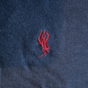 Mörkblå långärmad pikétröja Polo Ralph Lauren - Snygg mörkblå långärmad pikétröja från Polo Ralph Lauren med klassisk krage och knäppning framtill. Tröjan har det ikoniska röda broderade logotypen på bröstet och är tillverkad i mjuk bomull. Perfekt för en clean och stilren look.