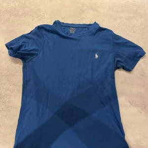 Blå t-shirt från Polo Ralph Lauren - Snygg blå t-shirt från Polo Ralph Lauren med klassisk vit broderad logga på bröstet.              T-shirten är tillverkad i mjuk bomull och har storlek S, passar runt 170cm. Hör gärna av dig vid frågor!