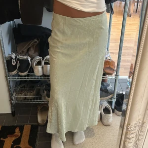 Ljusgrön blommig långkjol i satin - Supersnygg ljusgrön långkjol med subtilt blommigt mönster. Kjolen har en rak och flowy passform som sitter bekvämt i midjan. Materialet är glansigt satin som ger en lyxig känsla och snyggt fall. Perfekt för dig som gillar stilrena och trendiga plagg.