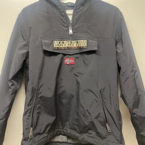 Svart vindjacka från Napapijri 162cm eller 14 - Svart vindjacka från Napapijri storlek 162cm eller 14. Har använts en del, men har inga skador eller defakter.