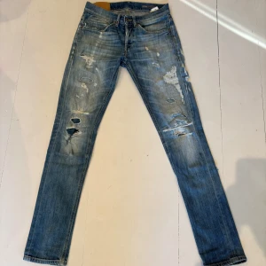 Blå skinny jeans från Dondup, stl 29 - Säljer ett par blå skinny jeans från George i storlek 29. Jeansen har slitna detaljer och hål på benen för en cool, avslappnad look. Klassisk femficksmodell med dragkedja och knapp. Perfekta för dig som gillar en smal passform och streetstil.