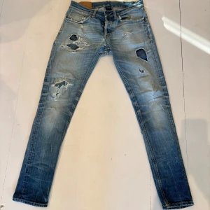 Ljusblå slitna jeans från Dondup - Säljer ett par ljusblå jeans från Diesel med flera slitningar och hål på benen för en riktigt edgy look. Jeansen har klassisk femficksdesign, knappgylf och smal passform. Tillverkade i bomull och perfekta för dig som gillar streetstyle. Lagade på flera ställen. Strl 33 men sitter som 31