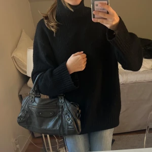 Svart stickad polotröja oversized - Mysig svart stickad polotröja med oversized passform och breda ribbade muddar vid ärmslut och hals. Perfekt för lager-på-lager och chill dagar. Hög krage som håller dig varm och ger en cool vibe.