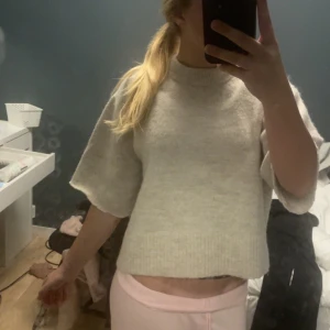 Beige stickad tröja med kort ärm - Supermysig beige stickad tröja med korta, vida ärmar och ribbad kant nertill. Tröjan har en rak, boxig passform och hög halsringning. Perfekt att slänga på sig för en chill och stilren look.