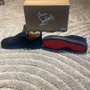 Christian Louboutin svarta mockasneakers - Snygga svarta sneakers från Christian Louboutin i mocka med klassisk röd sula. Lågt skaft, rund tå och svarta snören. Insidan är ljusbrun och skorna har diskret broderad logga på sidan. Perfekta för dig som vill sticka ut med exklusiva detaljer.