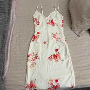 Vit blommig sommarklänning - Supersöt vit klänning med tunna axelband och blommigt mönster i rosa och rött. 