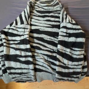 Zebramönstrad stickad tröja Esmara - Säljer en stickad tröja från Esmara med svart och grått zebramönster. Tröjan har en loose passform och ribbade muddar vid ärmslut och nederkant. Perfekt för dig som gillar djurmönster och vill ha något mysigt och snyggt till hösten eller vintern.