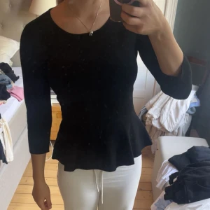 Svart peplumtop från Massimo Dutti - Svart peplumtop från Massimo Dutti med rund halsringning och trekvartsärm. Toppen har en figurnära passform upptill och en volangkant nedtill som ger en snygg siluett. Tillverkad i ett mjukt, strukturerat material som känns bekvämt mot huden.