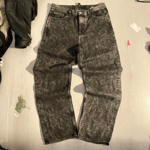 Weekday Galaxy Loose Straight Jeans - Säljer ett par Weekday Galaxy loose straight jeans i tvättad svart färg. De har hög midja, raka ben och en avslappnad passform. Jeansen är tillverkade i bomull och har klassiska fem fickor samt knappgylf. Perfekta för en chill och trendig look.
