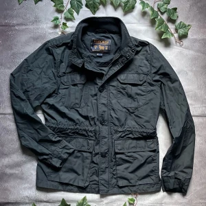 Woolrich “Mountain Field Jacket” Storlek L - Jackan har en lätt glansig yta, fyra framfickor, dold dragkedja och knäppning framtill samt justerbar midja för perfekt passform.  🎨 Färg: Svart 📏 Storlek: EU storlek L, USA storlek M (normal passform) 📐 Mått: Fråga ifall det önskas! ♻️ Skick: Mycket bra – minimala tecken på användning 🧵 Material: Polyamid / bomullsblandning  ‼️ Skickas dagen efter köpet genomförs! ‼️