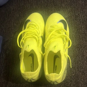 Nike Mercurial fotbollsskor neon - Säljer ett par Nike Mercurial fotbollsskor i en riktigt fet neongul färg med svarta detaljer och Nike-logga. Skorna har snörning och är designade för att ge max grepp på planen. Perfekta för dig som vill sticka ut och ha grym kontroll på bollen.