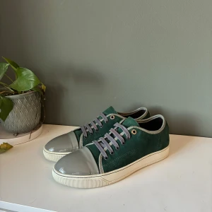 Gröna sneakers från Lanvin - Snygga gröna sneakers från Lanvin med grå snörning och en glansig grå tåhätta. Skorna har en vit sula och är perfekta för en stilren look. Passar bra till både vardag och mer uppklädda tillfällen.