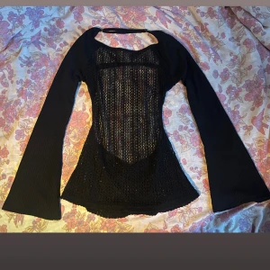 Svart långärmad topp - Säljer en svart långärmad topp med snygg spetsdetalj framtill. Toppen har en smickrande tight passform och ett öppet mönster på bröstet och magen som ger en cool look. Perfekt för dig som gillar att sticka ut med detaljer och stil.