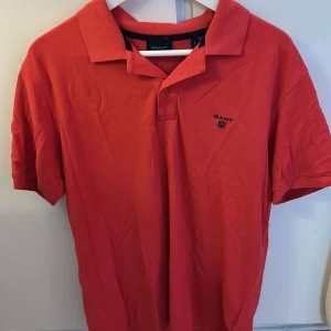 Röd pikétröja från GANT i bomull - Klassisk röd pikétröja från GANT med broderad logga på bröstet. Tröjan har krage, korta ärmar och är tillverkad i mjuk bomull. Perfekt för en stilren och avslappnad look.