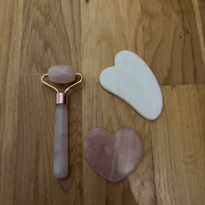 Rosenkvarts roller & gua sha set - Säljer ett set med ansiktsroller och två gua sha-stenar i rosenkvarts och vit jade. Rollern har ett handtag i ljusrosa sten med roséguldfärgade detaljer. Gua sha-stenarna är hjärtformade, en i ljusrosa rosenkvarts och en i vit jade, perfekta för ansiktsmassage och glow. Använda en gång, som i nyskick