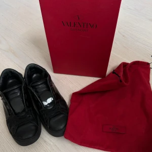 Svarta Valentino Garavani sneakers - Säljer ett par helsvarta Valentino Garavani sneakers i skinn med klassisk låg siluett och snörning. Skorna har en chunky sula och diskreta detaljer, levereras med originalkartong och dustbag. Perfekta för dig som gillar lyxiga och stilrena sneakers.