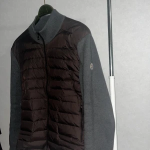 Moncler tricot cardigan  - M/L använd 2 gånger bara Säljer en stilren pufferjacka från Moncler i grått och svart. Jackan har quiltad framsida i svart med dragkedja och två fickor, samt grå stickade ärmar och rygg. Perfekt för dig som vill ha en snygg och bekväm jacka med sportig känsla.