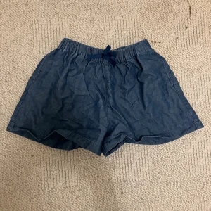 Blå shorts med snörning från Uniqlo - Snygga blå shorts från Uniqlo med elastisk midja och snörning framtill. De är tillverkade i mjukt bomullsmaterial och har en loose passform som gör dem sköna att bära. Perfekta för varma dagar och chill häng. Fickor på sidorna för extra funktion.