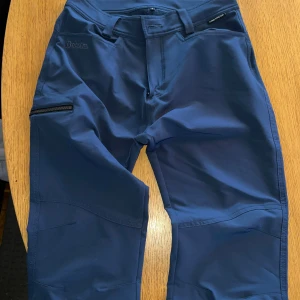 Blå funktionsbyxor från Dobsom, stl S - Säljer ett par blå funktionsbyxor från Dobsom i storlek S. Byxorna har en smidig dragkedjeficka på benet och är tillverkade i ett stretchigt syntetmaterial som passar perfekt för utomhusaktiviteter. Snygg och sportig look med modern passform.
