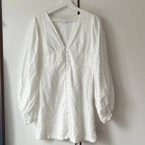 Vit klänning från Vila - Superfin vit kortklänning från Vila med v-ringning, långa puffärmar och dekorativa knappar framtill. Den har endast används en gång och det va på min student:). Den va dn maxi klänning från början som sen syddes upp till en kort klänning