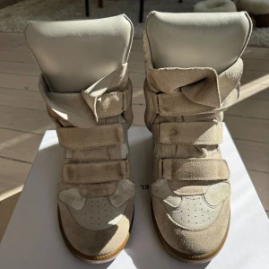 Isabel Marant Bekett Sneakers - Säljer mina snygga och sköna Isabel Marant Bekett sneakers med klack i färgen Ecru för att dom inte längre kommer till användning! Skorna är i bra skick, dock använda så lite smutsiga, se bilder. Annars fina utan defekter. Storlek 41, men passar mig bra som vanligtvis har storlek 40. Kartong medföljer😇🌸