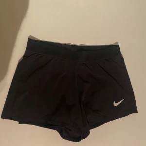 Svarta träningsshorts från Nike - Svarta träningsshorts från Nike med klassisk vit logga på ena benet. De har undershorts och är super bra att träna i. BARNSTORLEK