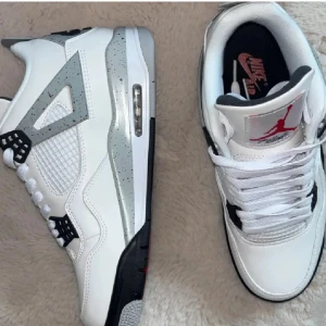 Nike Air Jordan 4 Retro White Cement - Nike Air Jordan 4 Retro White Cement med vit ovandel i skinn, grå och svarta detaljer samt röda accenter. Klassisk meshpanel på sidorna, synlig Air-enhet i sulan och specklad grå midsole. Ikonisk Jumpman-logga på plösen och Nike Air på hälen. Grymma sneakers för dig som gillar streetstyle.