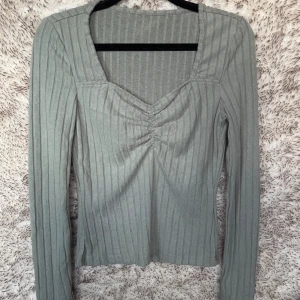 Grön ribbad långärmad topp - Snygg grön ribbad topp med lång ärm och v-ringning.. Toppen har rynkade detaljer vid bysten och är tillverkad i ett mjukt och stretchigt tyg.
