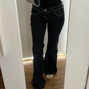 Ultra low flare jeans i mörk denim - Säljer ett par ultra low flare jeans från Ginatricot i mörkblå denim. Byxorna har låg midja, utsvängda ben och tydliga kontrastsömmar. Klassisk femficksmodell med knapp och dragkedja framtill. Perfekta för en trendig och avslappnad look. Helt nya och oanvända, jag är 1,58 för referens.