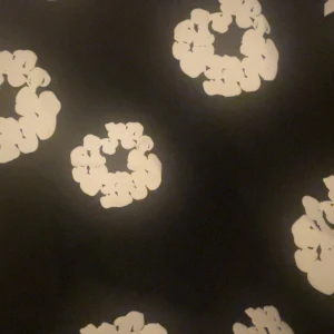 Svart tröja med vita blommor Denim Tears - Svart tröja från Denim Tears med stora vita blommor i ett mönster över hela plagget. Tröjan har en klassisk passform och är perfekt för dig som vill sticka ut med en unik och trendig stil.