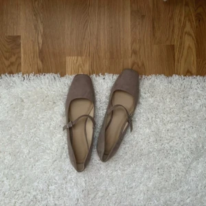Beige Mary Jane ballerinaskor H&M - Beige ballerinaskor från H&M i Mary Jane-modell med fyrkantig tå och smal passform. Skorna har en snygg rem med spänne över foten och är gjorda i mockaliknande syntetmaterial. Endast använda en gång. Slutsålda online. Orginalpris: 249