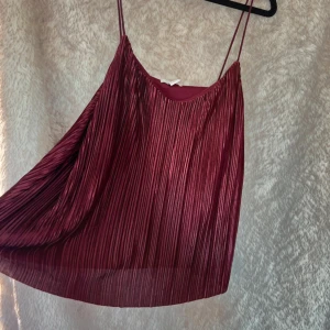 Plisserad vinröd linnetopp - Säljer en vinröd plisserad linnetopp med tunna axelband. Toppen har ett glansigt tyg.