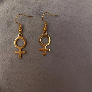 Feminist örhängen guld imitation kvinnosymbolen - 10% av det här köpet ger jag till kvinnojouren Karlskrona.   Fina örhängen med kvinnosymbolen. Guldimitation. 