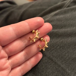 Guldiga örhängen med spikes - Unika örhängen i guldtonad metall med coola spikes runt hela ringen. De är små och har en halvcirkelformad design som ger en edgy vibe. Perfekta för dig som vill sticka ut med din stil och gillar detaljer som syns.