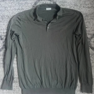 Mörkgrå pikétröja från John Henric - Snygg mörkgrå långärmad pikétröja från John Henric. Tröjan har klassisk krage, två knappar vid halsen och ribbade muddar vid ärmslut och nederkant. Perfekt för dig som gillar stilrena och enkla plagg.