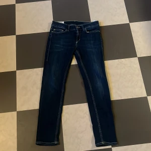 Blå Dondup jeans, storlek 29 - Snygga blå jeans från Dondup med klassisk femficksdesign och kontrastsömmar. Jeansen har raka ben och coola detaljer på bakfickorna samt läderpatch med logga i midjan. Perfekta för dig som gillar stilrena och tidlösa jeans.